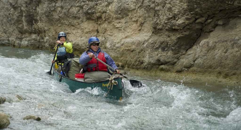 two people paddle a canoe through whitewater on an outward bound gap year course